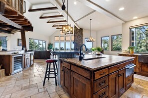 A spacious kitchen with a large island, wooden cabinetry, and a stone accent wall. - Spacious 6700 SQFT Home | 4 Ensuite Bedrms + Kids Bunkrm + Game Rm + Media Room (Powell Butte)