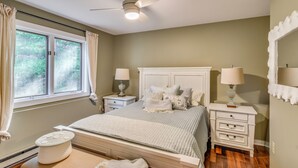 Un dormitorio con cama, mesitas de noche, ventilador de techo y una ventana con cortinas.