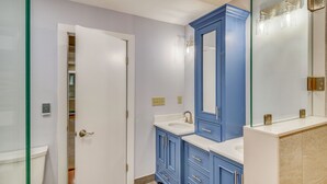 Un baño con inodoro blanco, tocador azul con espejo y cabina de ducha de vidrio.