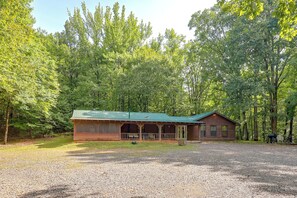 Eine Hütte mit Veranda und Kopfsteinpflasterauffahrt, umgeben von einem Wald.