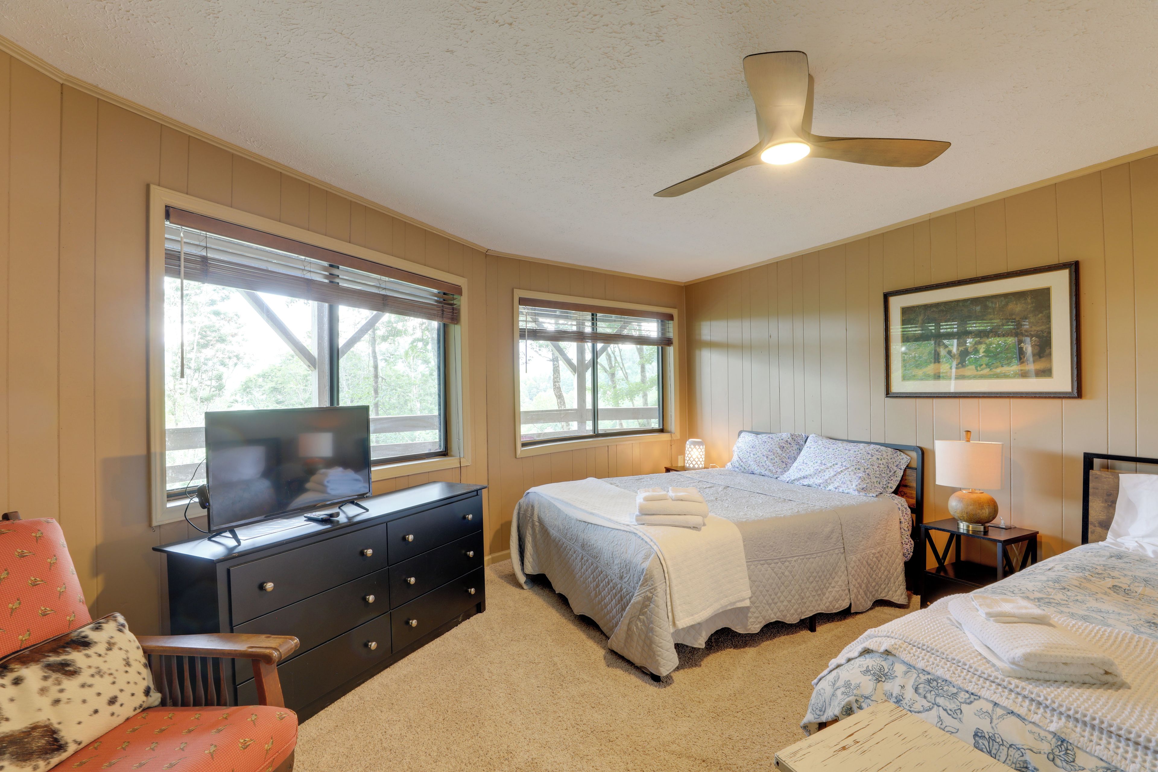 A bedroom with a bed, a dresser, a chair, a television, and a ceiling fan.