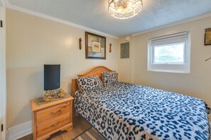 A bedroom with a bed, a nightstand, a wall-mounted light fixture, a window with blinds, and a framed picture on the wall.