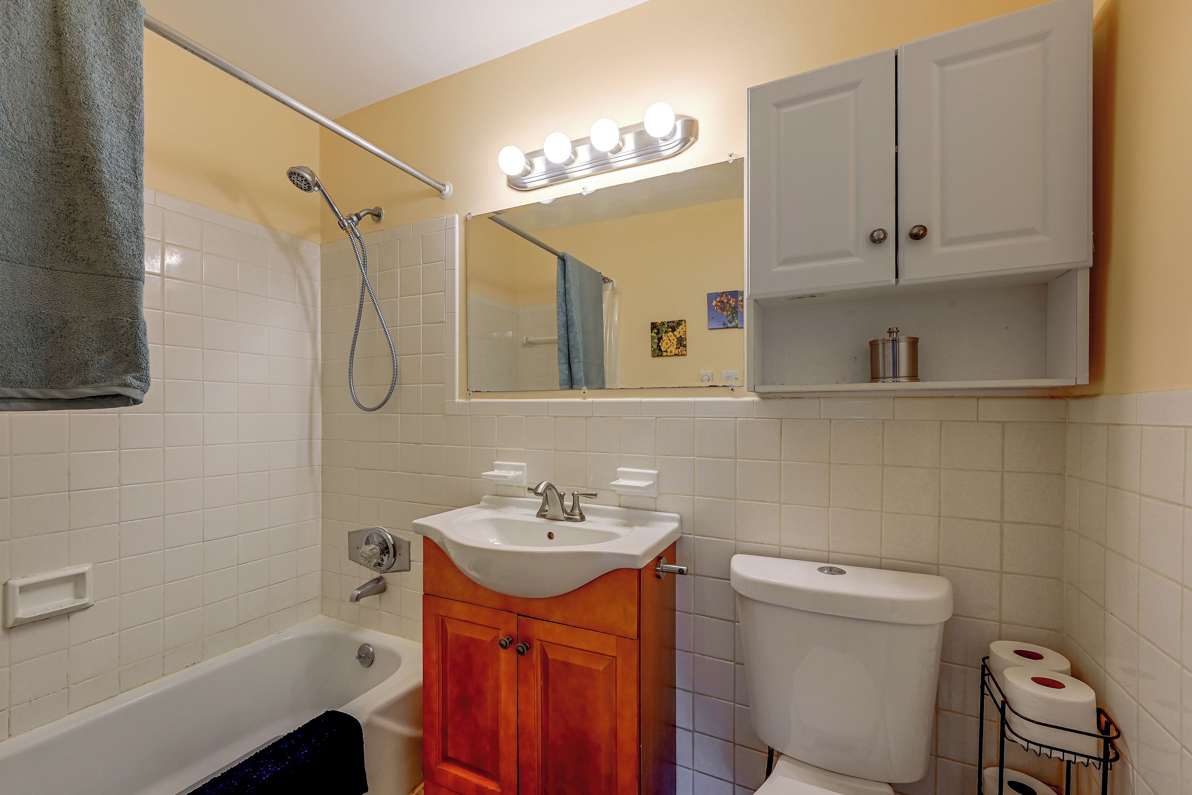 A bathroom with a bathtub, a sink, a toilet, and a mirror with lights above it.