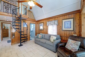 Ein Holzinnenraum mit einer Treppe, einem grauen Sofa, einem Ledersessel und einem Deckenventilator.
