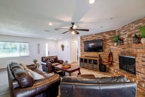 A spacious living room with a leather sofa, a television mounted on a brick wall, and a ceiling fan. - Winter Haven Chain of Lakes Getaway Near Legoland (Winter Haven)