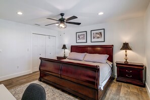 A bedroom with a wooden bed, a ceiling fan, two bedside lamps, a nightstand, a dresser, and two framed pictures on the wall. - Winter Haven Chain of Lakes Getaway Near Legoland (Winter Haven)