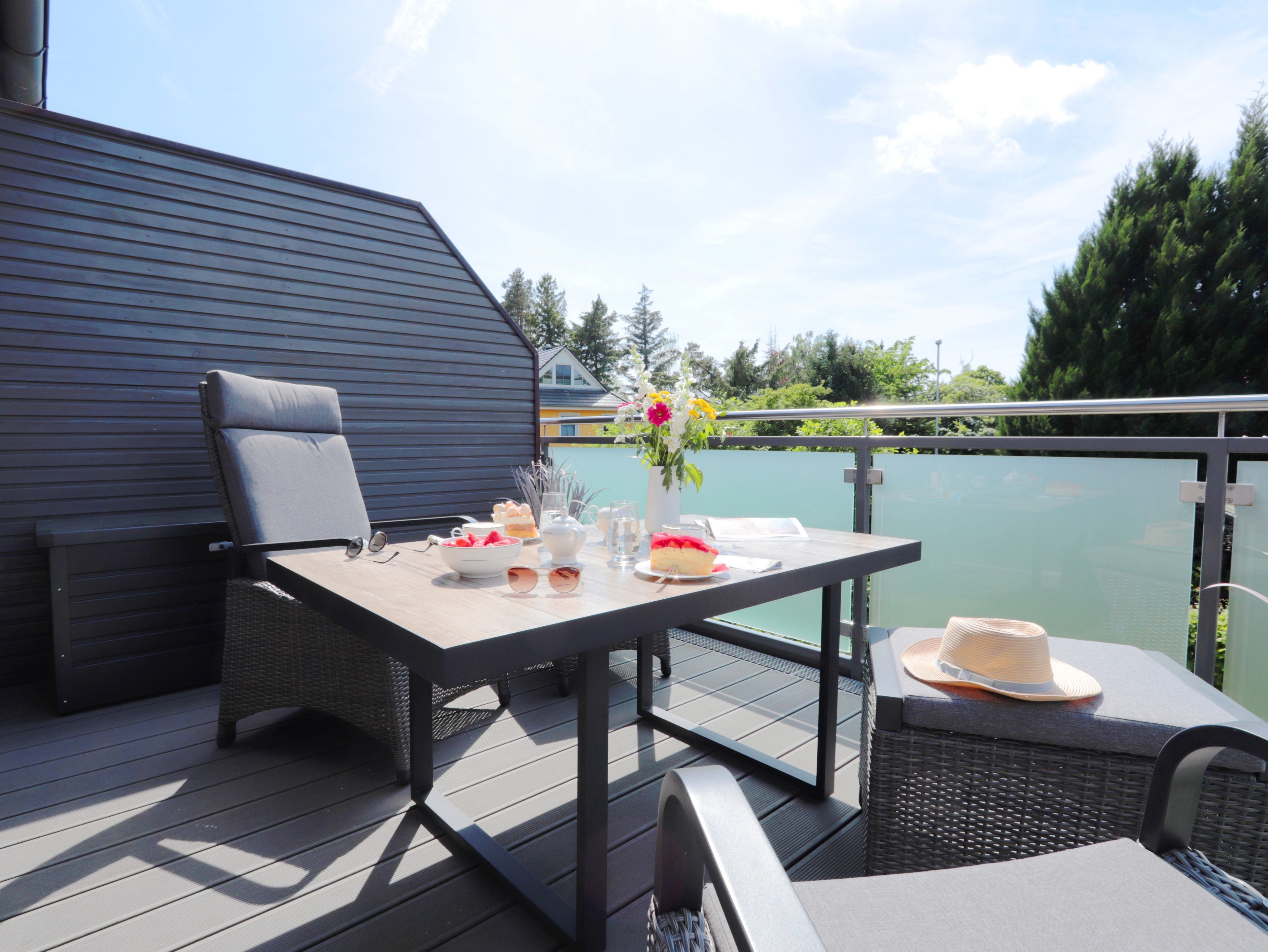Una terraza con mesa dispuesta para una comida, mobiliario exterior y vista a un cuerpo de agua.