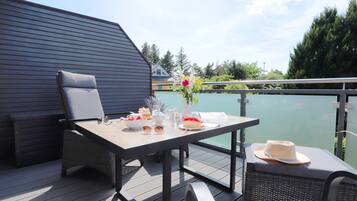 Una terraza con mesa dispuesta para una comida, mobiliario exterior y vista a un cuerpo de agua.