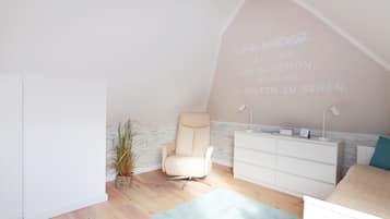Una habitación con techo inclinado, una silla blanca, un tocador blanco, una planta pequeña y una alfombra azul claro.