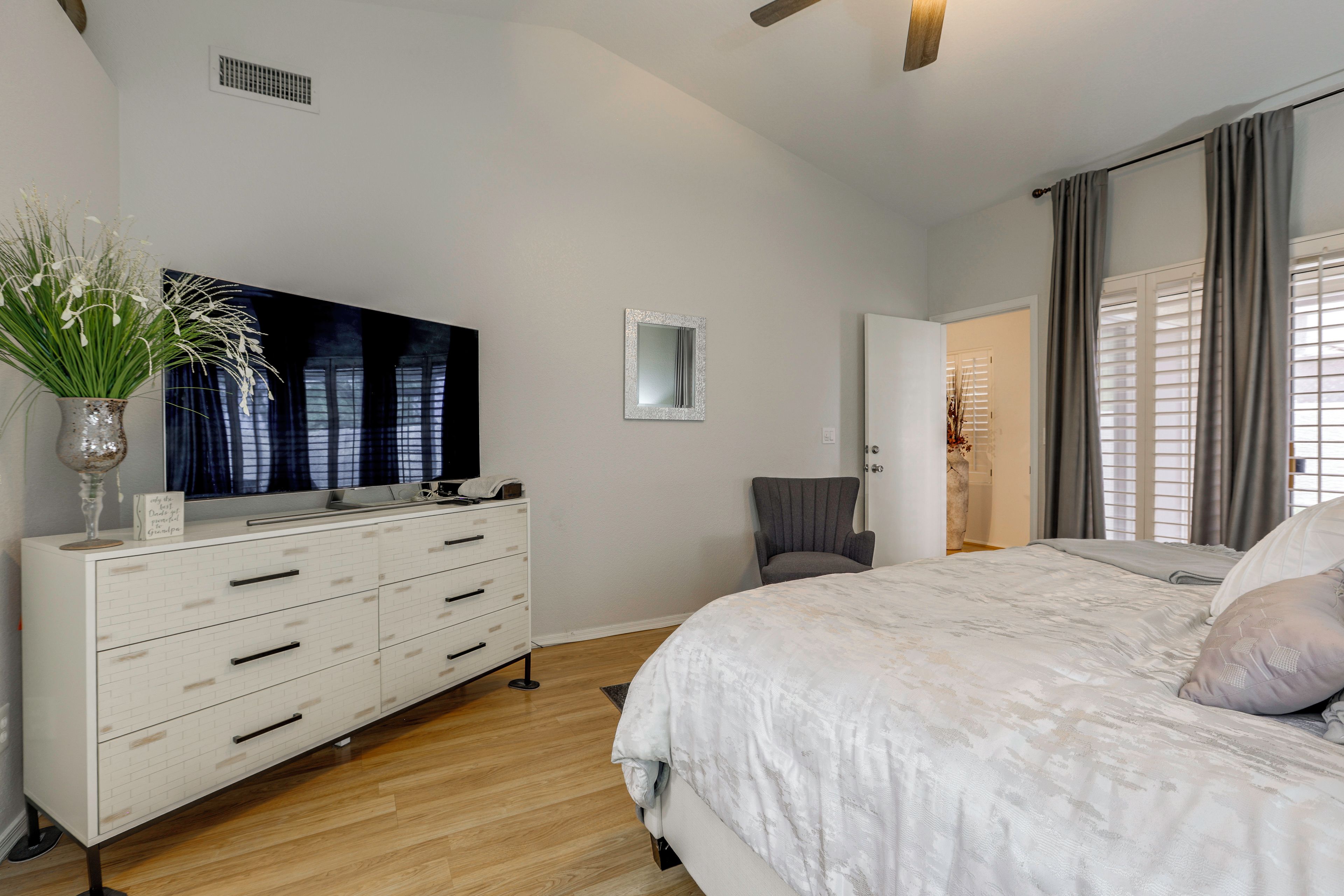 Een slaapkamer met een groot bed, een dressoir, een flatscreen televisie en een spiegel.