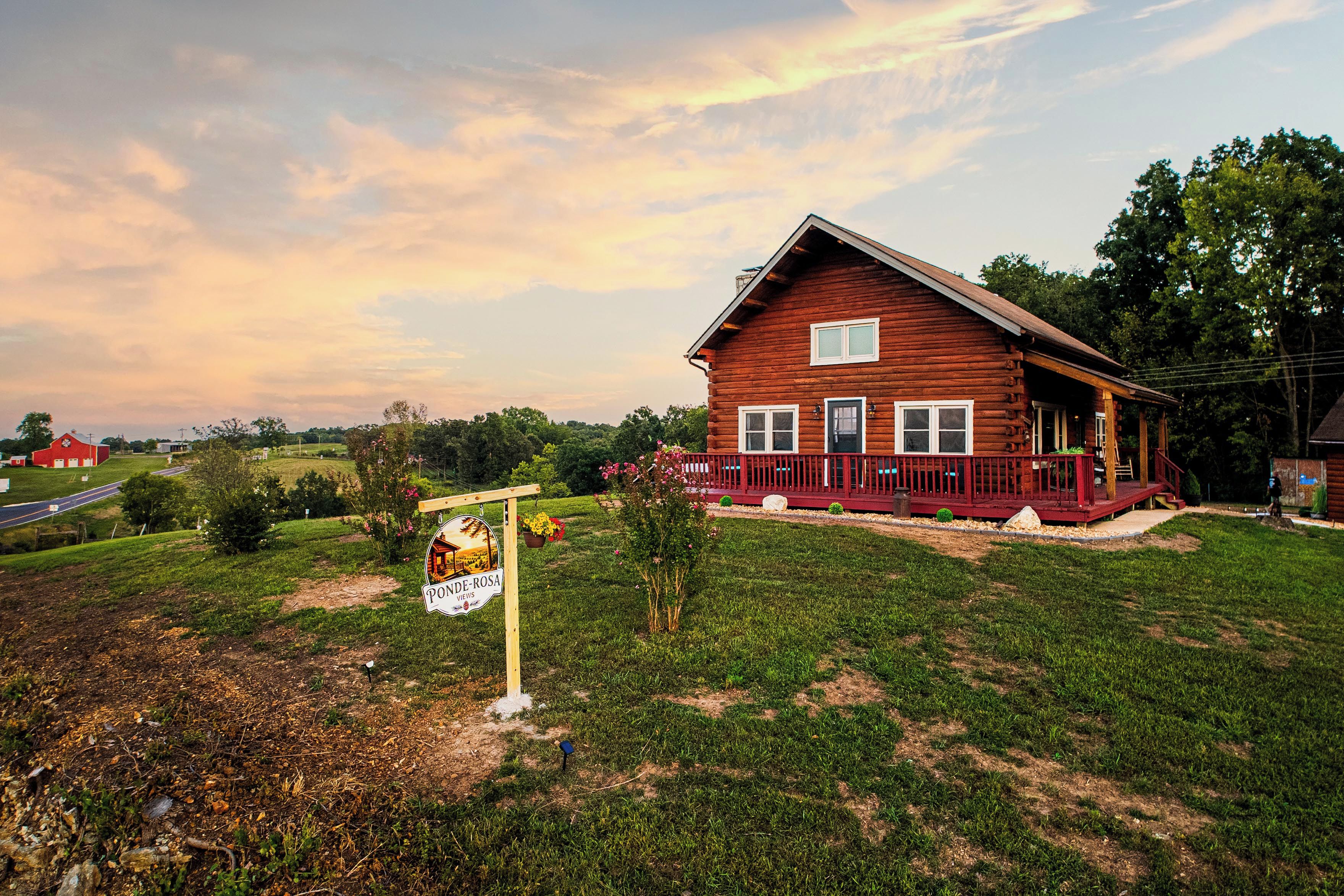 A wooden house with a porch, surrounded by a grassy yard and a sign indicating 'PONDE-ROSA VIEWS'.