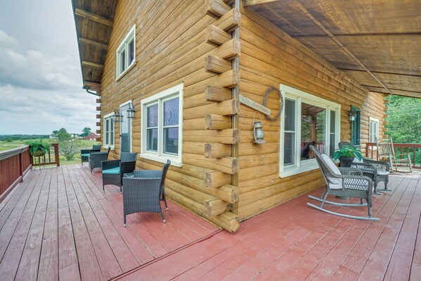 A log cabin with a deck, wicker furniture, and a view of the landscape.