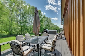 Eine Terrasse im Freien mit Tisch, Stühlen, einem Grill und Blick auf die grüne Umgebung.