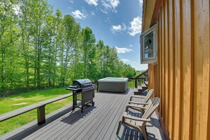 A wooden deck with a grill, hot tub, and lounge chairs.
