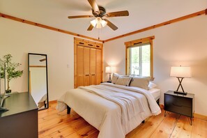 Ein Schlafzimmer mit Bett, Nachttischen, Deckenventilator, Fenster und Holzboden.