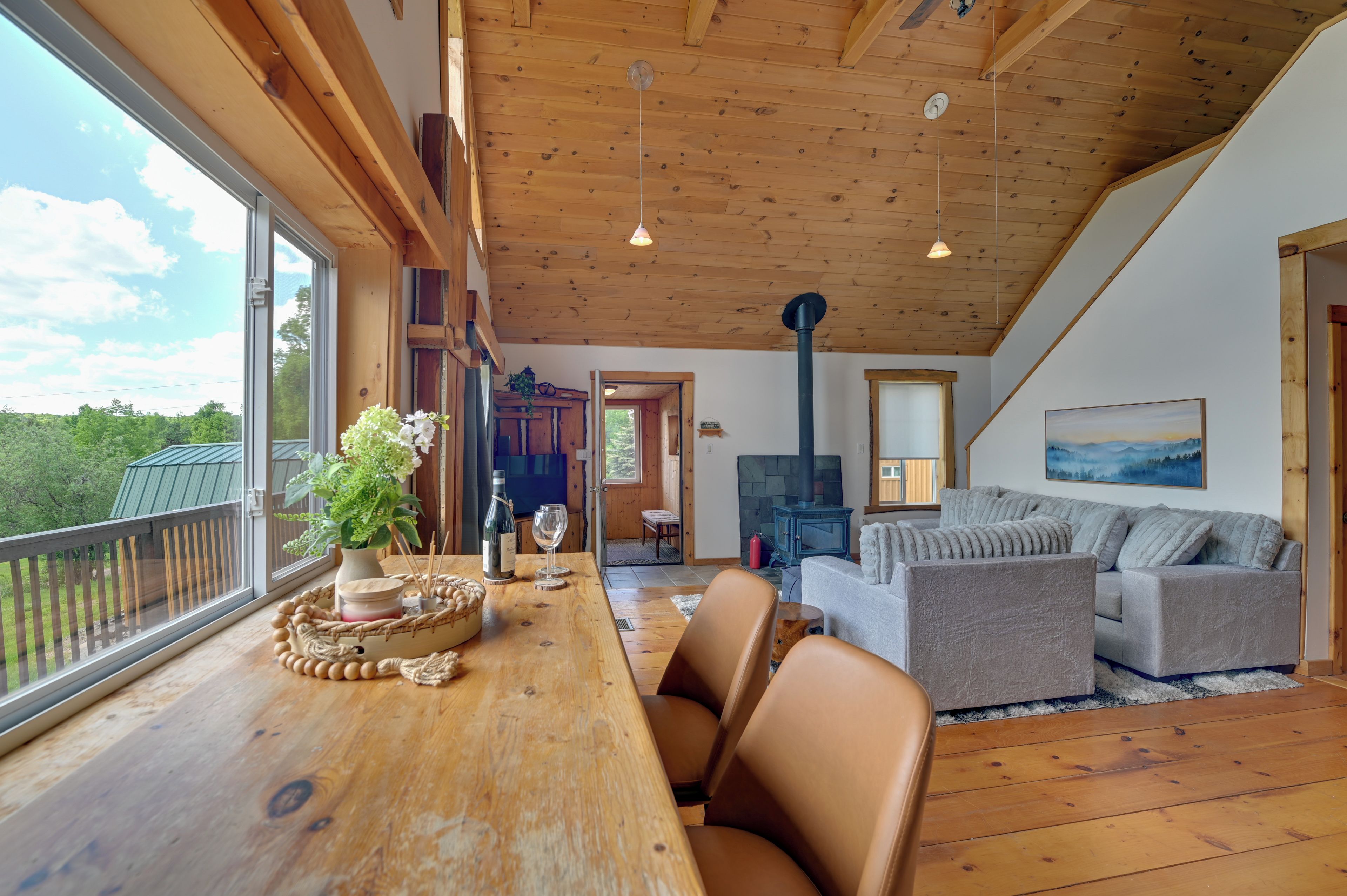 A spacious living area with a wooden ceiling, a fireplace, and a large window overlooking a deck.