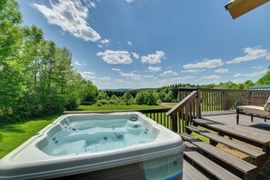 Ein Whirlpool auf einer Holzterrasse mit Blick auf eine grüne Landschaft und Bäume.