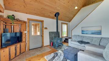 A cozy living room with a wooden ceiling, a television on a wooden cabinet, a sofa, a rug, and a fireplace.