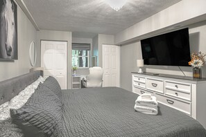 Quarto com cama grande, cômoda, televisão e janela.