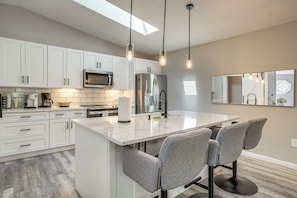 A modern kitchen with white cabinets, a central island with bar stools, stainless steel appliances, and pendant lighting. - Massanutten Resort Home w/ Hot Tub & Game Room! (McGaheysville)