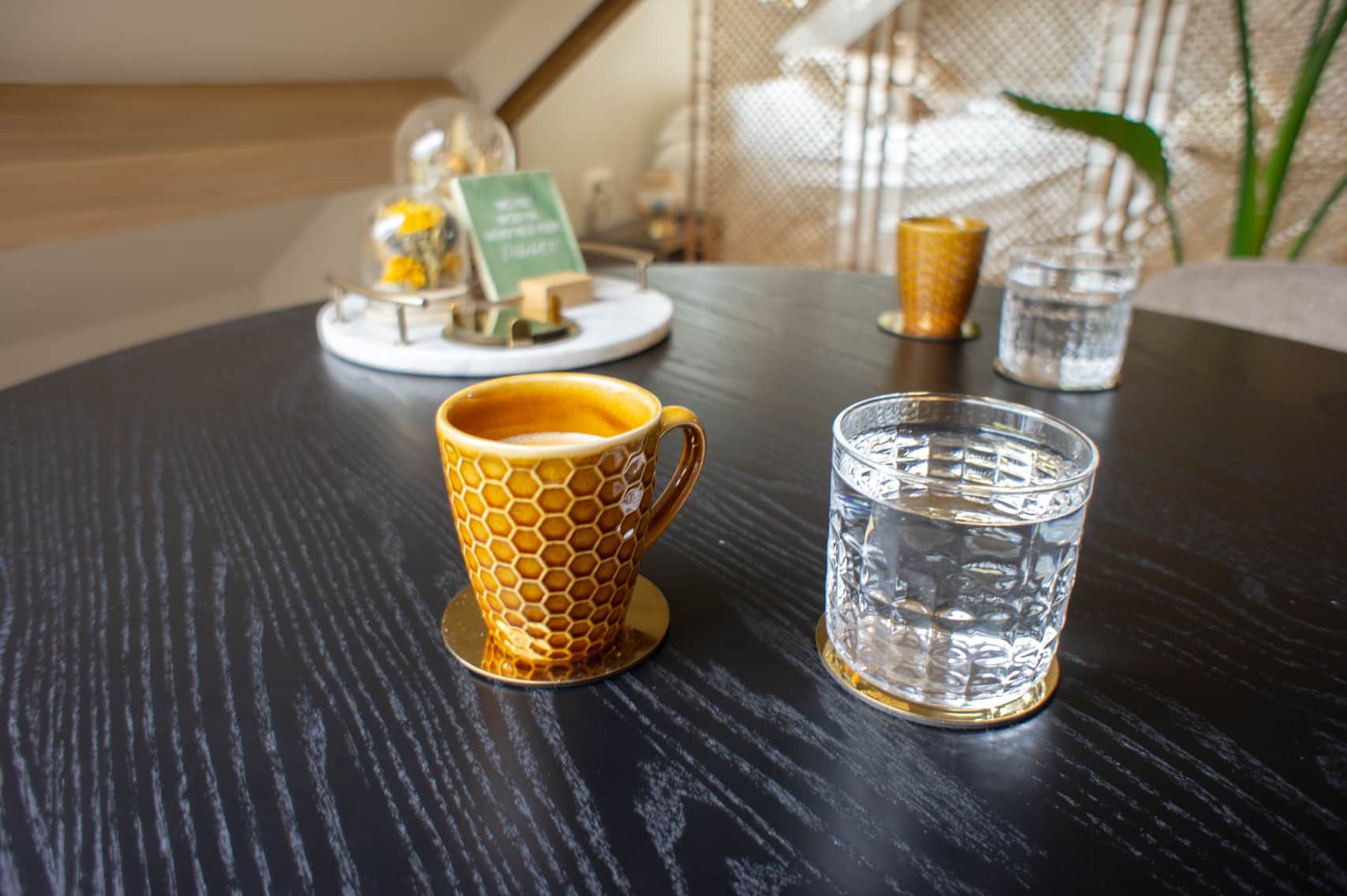 A table with a coffee cup and a glass of water, a menu stand, and a decorative item in the background.