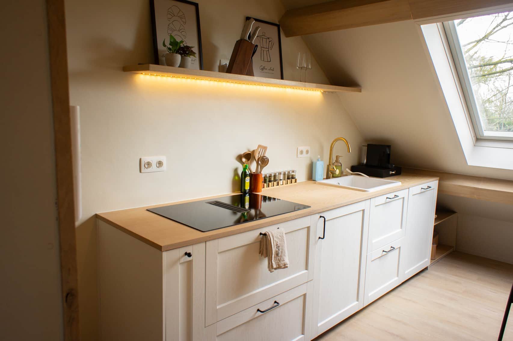 A modern kitchen with a black induction cooktop, white cabinetry, and a window above the sink.