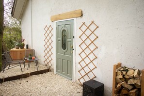 A door with a lattice, a chair, a table, and a stack of firewood against a wall.