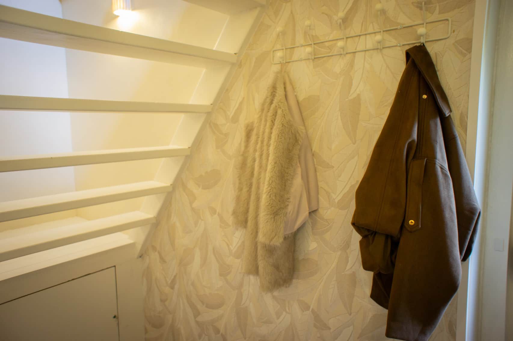 Une pièce avec un papier peint à motifs, une serviette suspendue et un porte-manteau sur lequel est accroché un manteau.