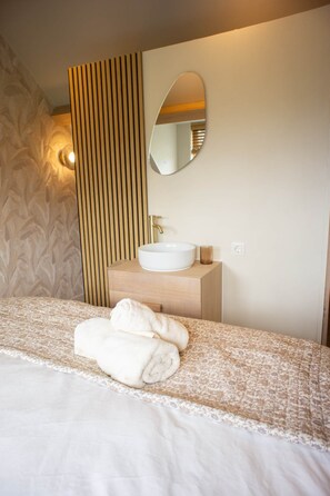 Habitación de hotel con una cama, un lavamanos blanco, un espejo y una pared con listones de madera verticales.