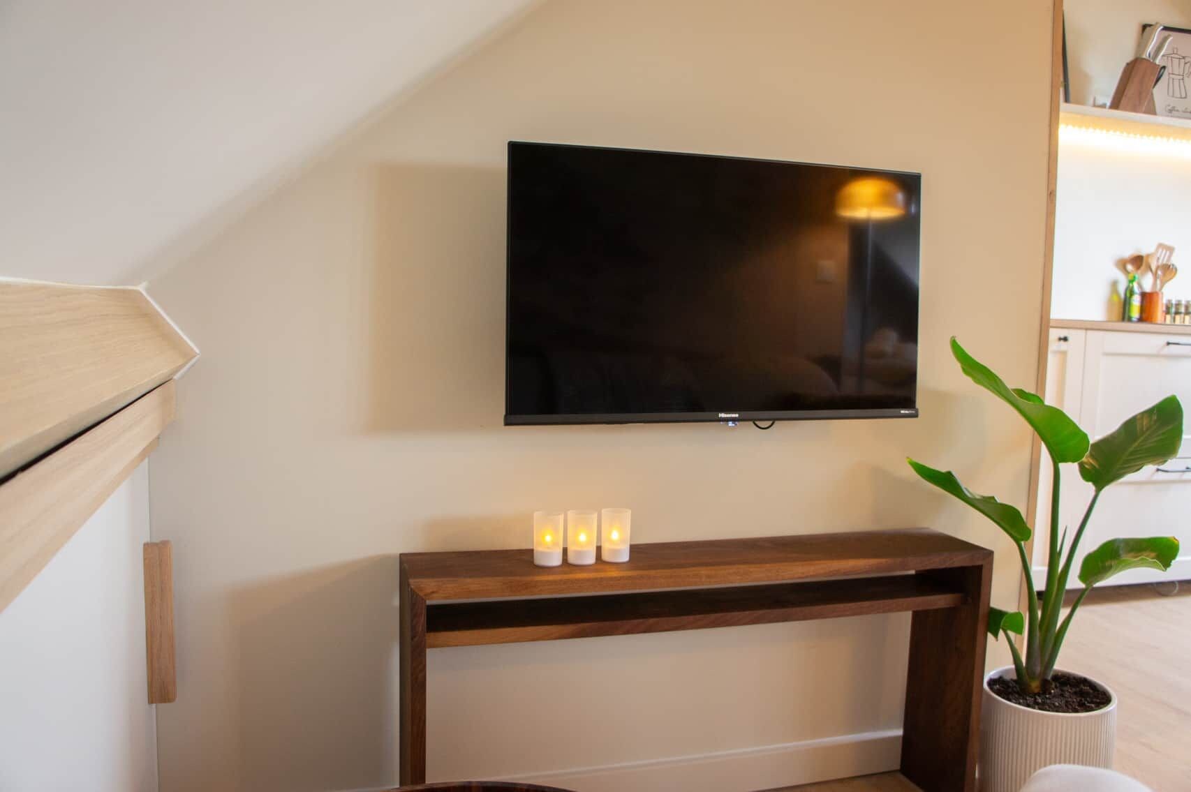 Un televisor de pantalla plana montado en la pared sobre un mueble consola de madera con tres velas encendidas.