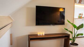 Un televisor de pantalla plana montado en la pared sobre un mueble consola de madera con tres velas encendidas.