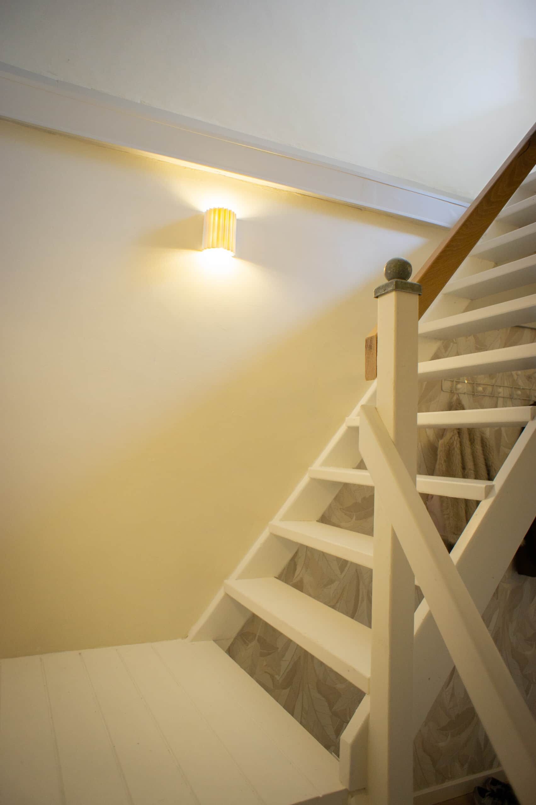 Een trap met witte leuningen en een houten handrail, leidend naar een plateau met een lamp.