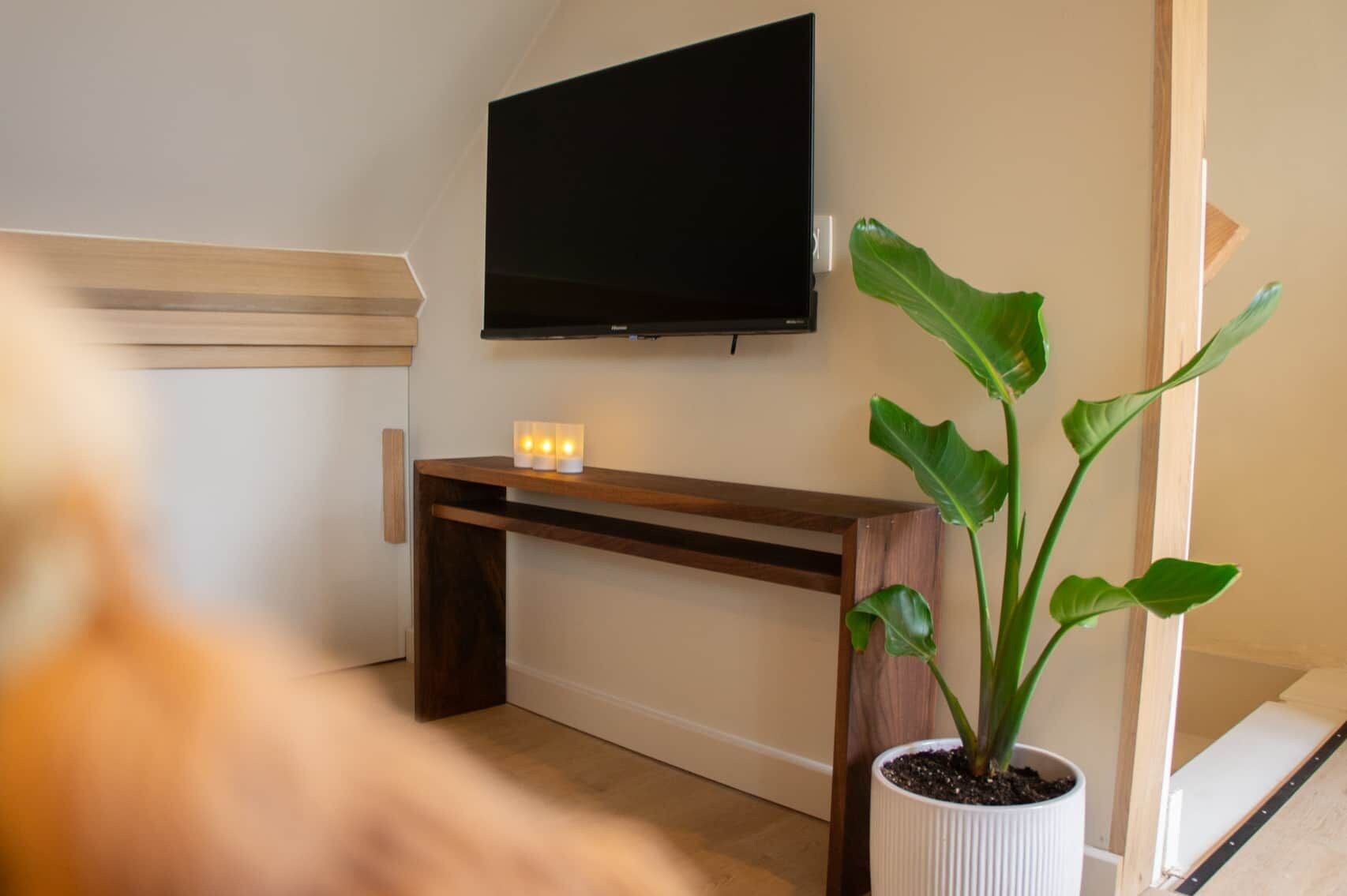 A room with a flat-screen TV mounted on the wall, a wooden bench, and a potted plant.