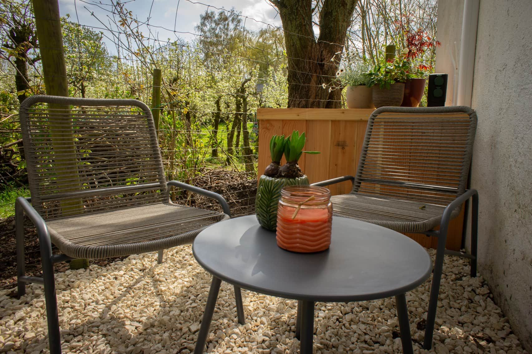 Een terras met twee rieten stoelen, een kleine ronde tafel en een potplant.