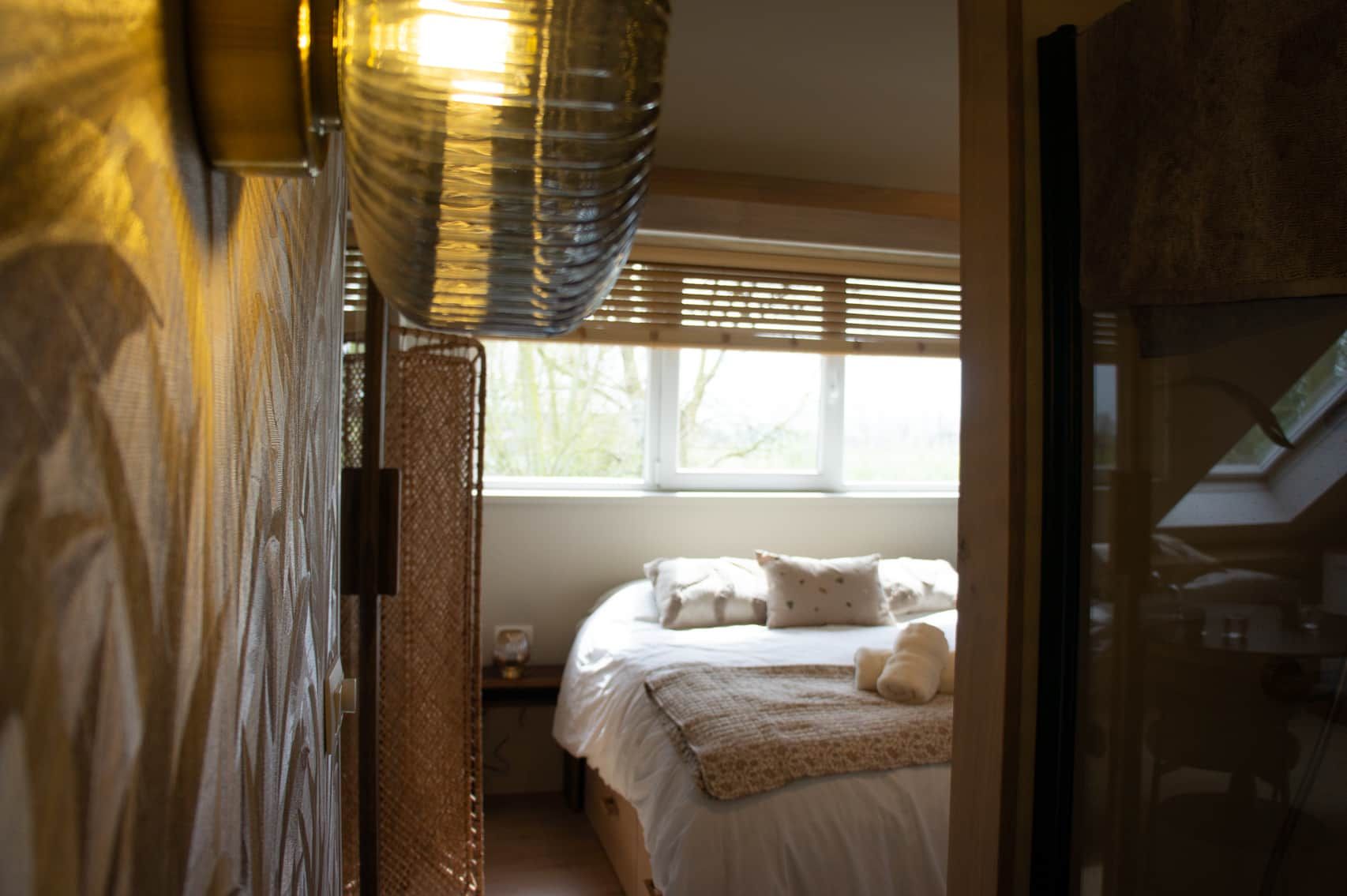 Une chambre à coucher avec un lit, des oreillers, une table de chevet et une fenêtre avec des stores.
