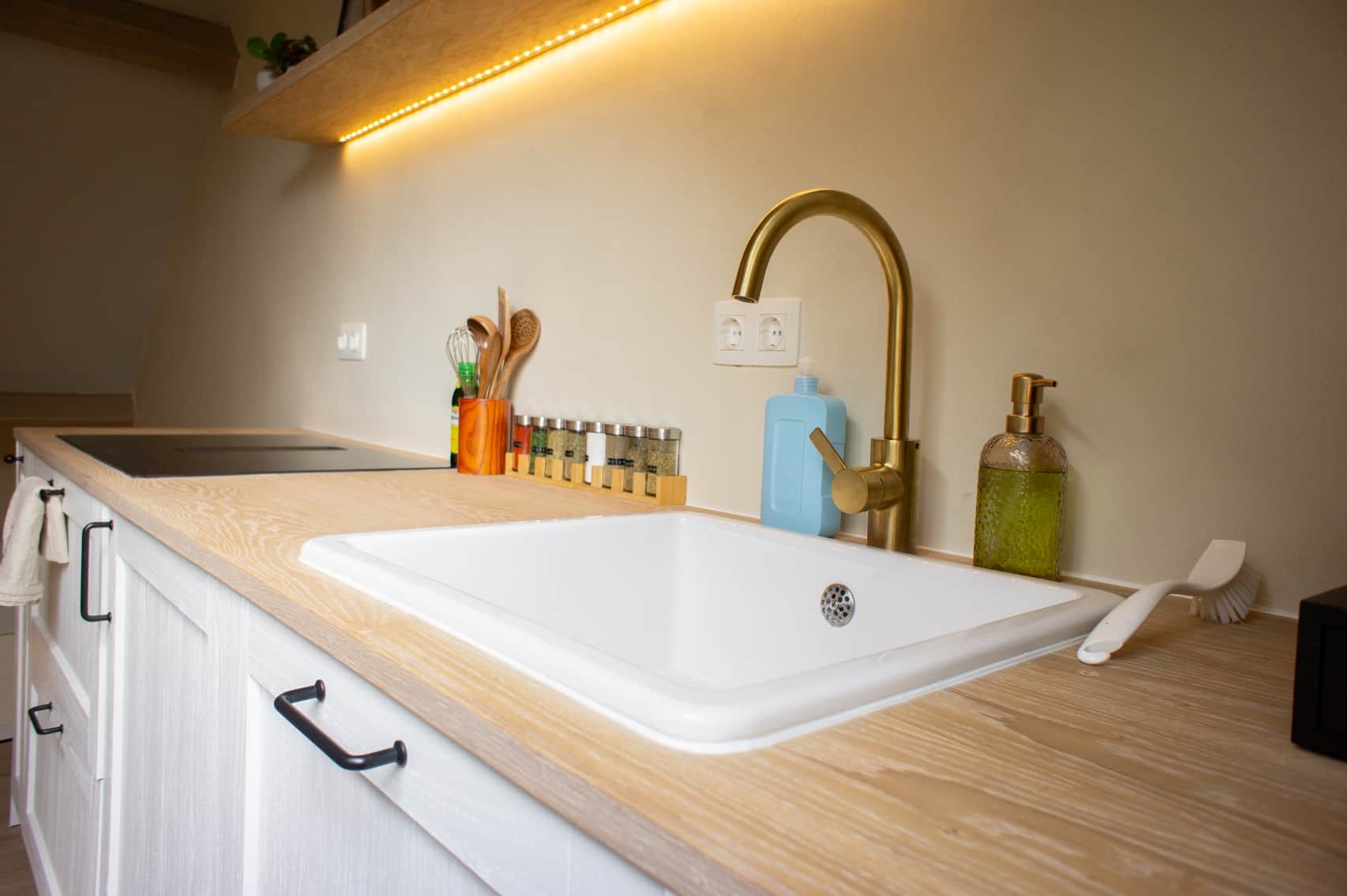 A kitchen with a white sink, a brass faucet, and a wooden countertop.