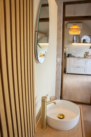 Un baño moderno con un lavamanos blanco, grifo dorado y espejo con marco verde.
