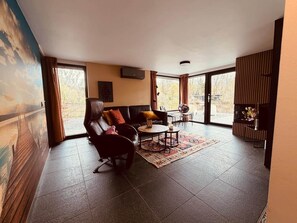 A modern living room with a leather sofa, a round coffee table, and a large window offering a view of the outdoors. - Bunga Vijverzicht (Bunga holidays) (Lanaken)