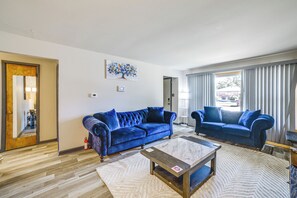 Una sala de estar con dos sofás azules, una mesa de centro, un cuadro en la pared y una puerta que da a otra habitación.