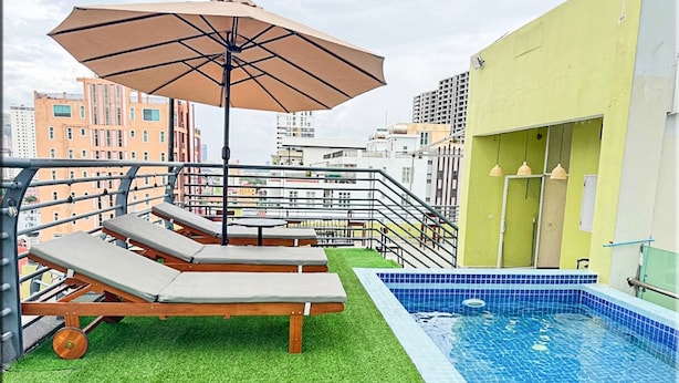 A rooftop pool area with lounge chairs and an umbrella, surrounded by city buildings. - The Movie Hotel by Mecon (Phnom Penh)
