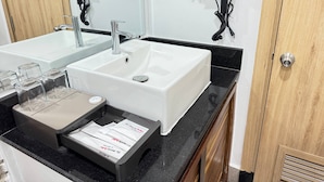 A bathroom with a white sink, a mirror, a black countertop, and a wooden door. - The Movie Hotel by Mecon (Phnom Penh)