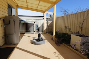A covered patio area with a water heater, a gate, and a small garden with plants and a tree.