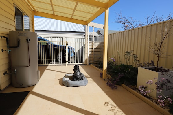 A covered patio area with a water heater, a gate, and a small garden with plants and a tree.