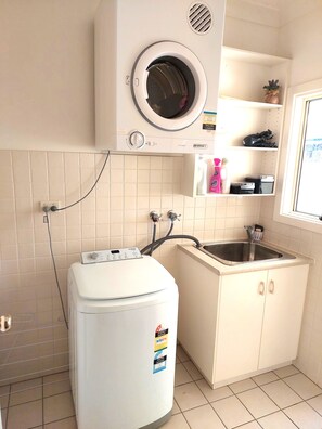 A compact laundry area with a front-loading washing machine, a built-in dryer, and a sink with a countertop.