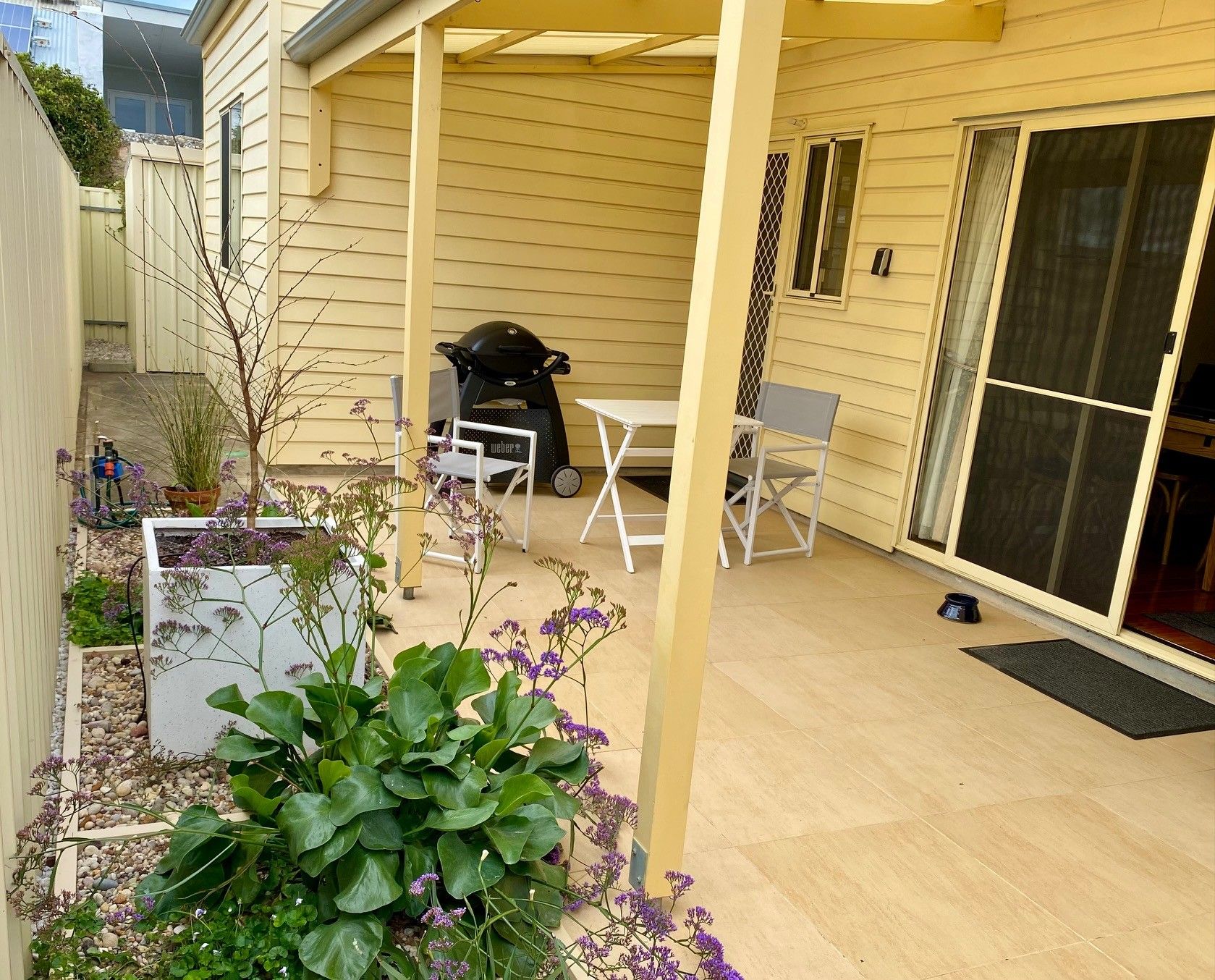 Un patio couvert comprenant un barbecue, des sièges et des plantes en pot.
