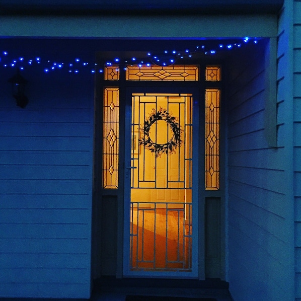 A house entrance with a decorative door, a wreath, and blue string lights.