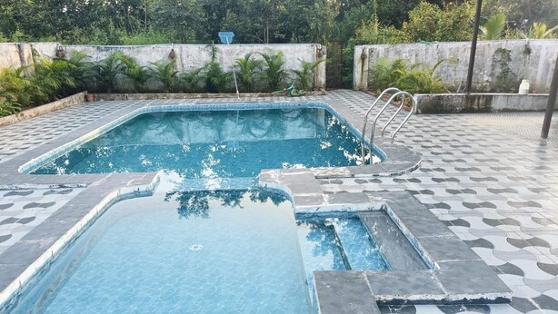 A swimming pool with a tiled deck and a metal ladder. - Tulip Garden And Resort (Bichhiya)