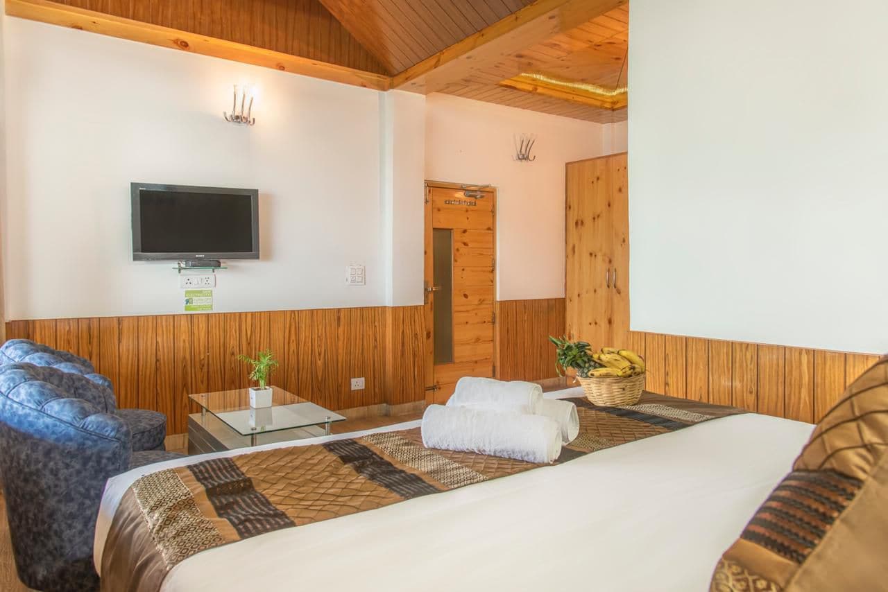 A hotel room with a bed, a television, a wooden wall panel, a door, and a small table with a plant.