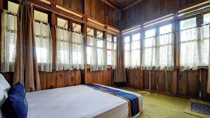 Een kamer met een groot bed, houten wanden en meerdere ramen met gordijnen.