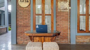 Een receptiegedeelte met een houten tafel, twee geweven zitkussens, een Lenovo laptop en borden aan de muur.